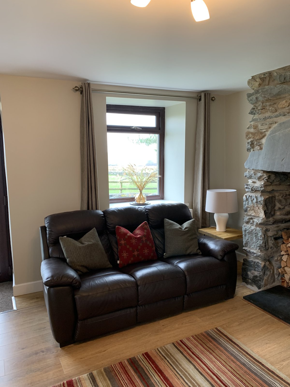 Leather sofa beside the stone fireplace in the living room, with a window looking out over the fields